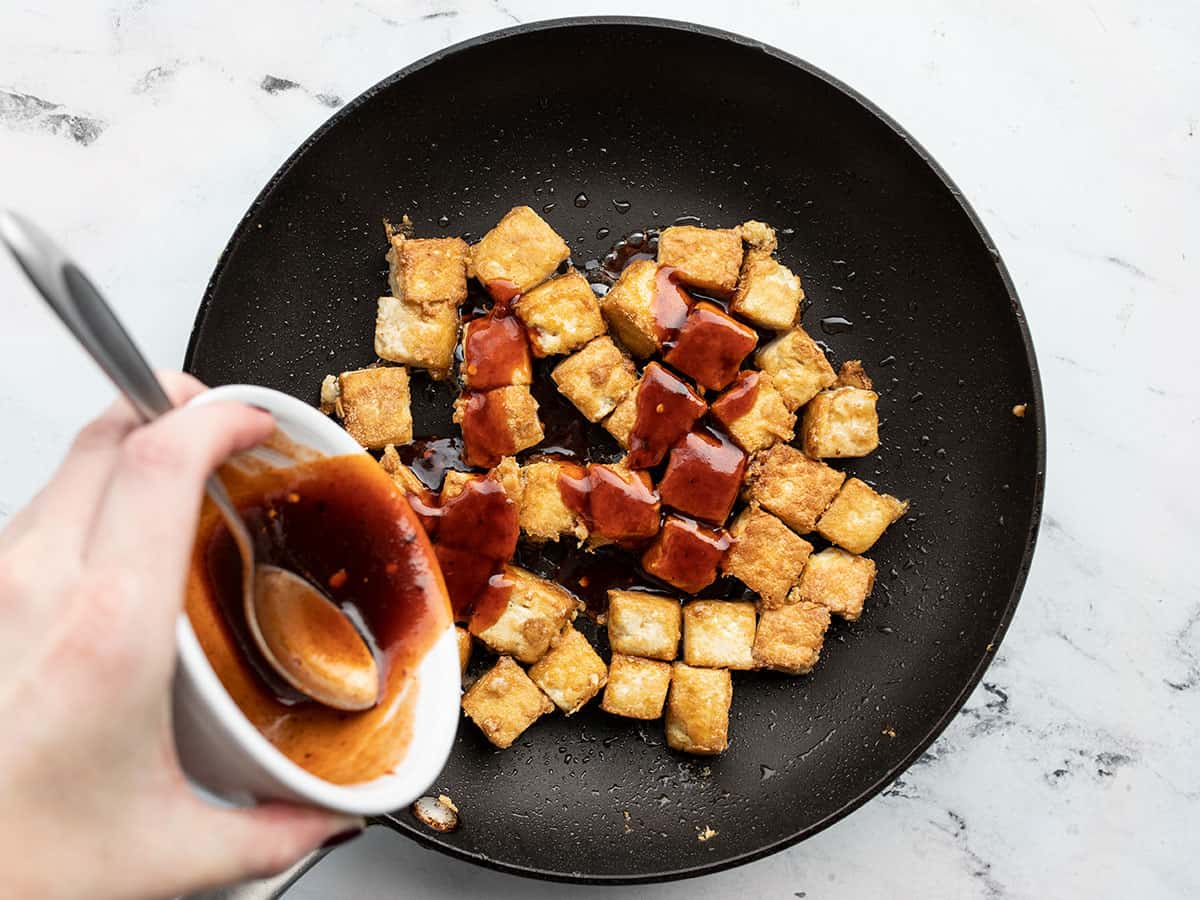 honey sriracha sauce being poured over the tofu in the skillet