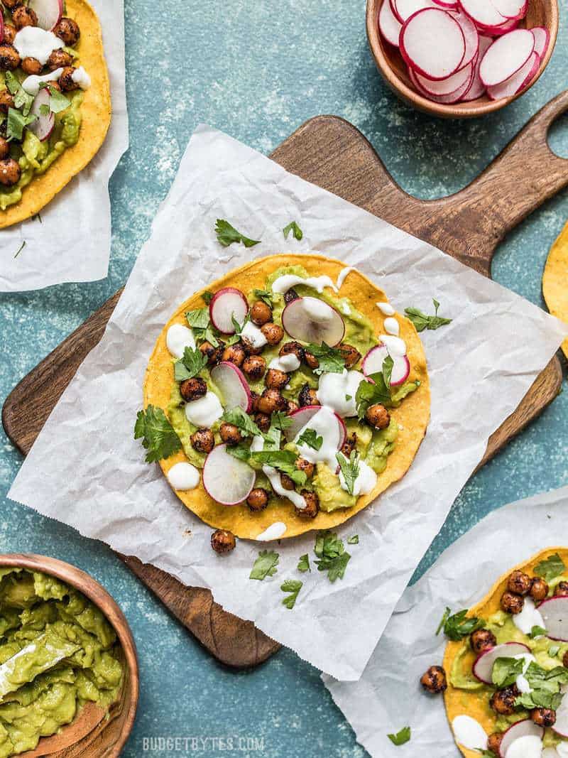 Spiced Chickpea Tostadas on pieces of parchment and a wooden cutting board