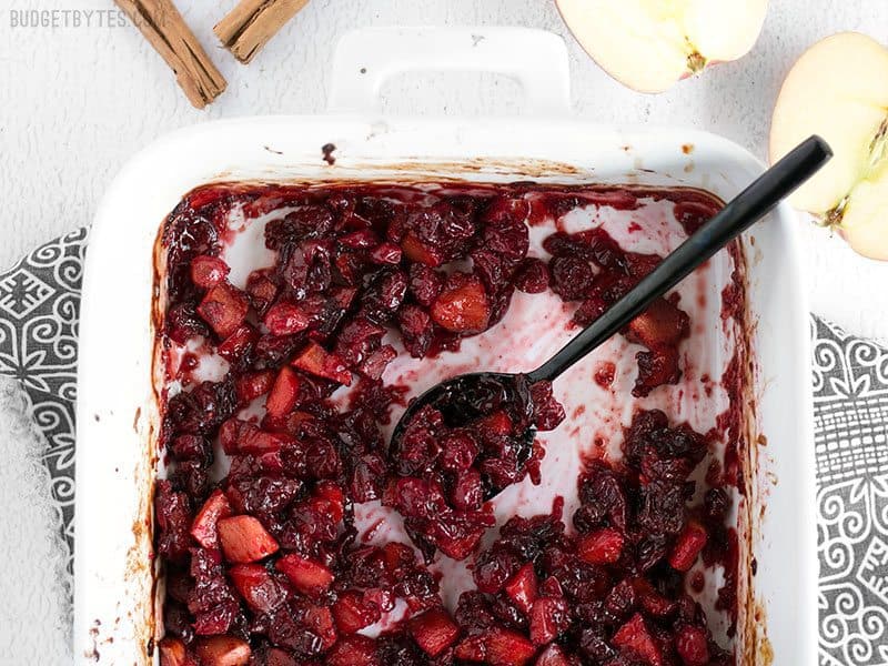 Roasted Apple Cranberry Relish being scooped out of the casserole dish with a black spoon.