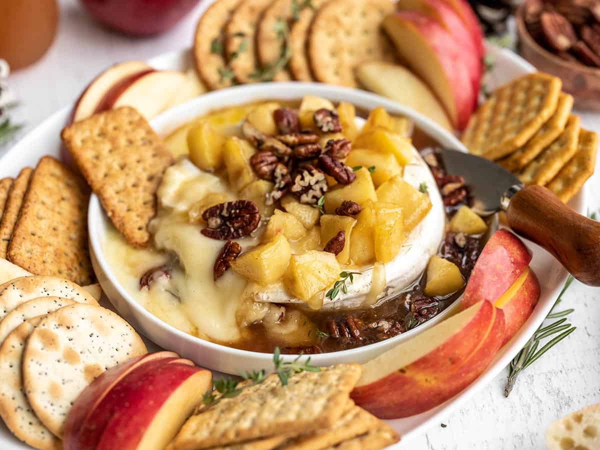 Side view of baked brie with apples surrounded by crackers and apples