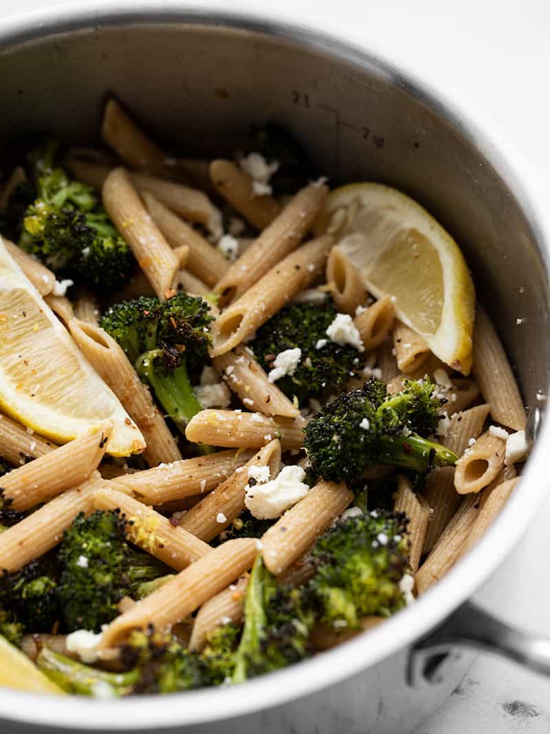 Front view of a pot full of Roasted Broccoli Pasta with Lemon and feta, garnished with lemon wedges