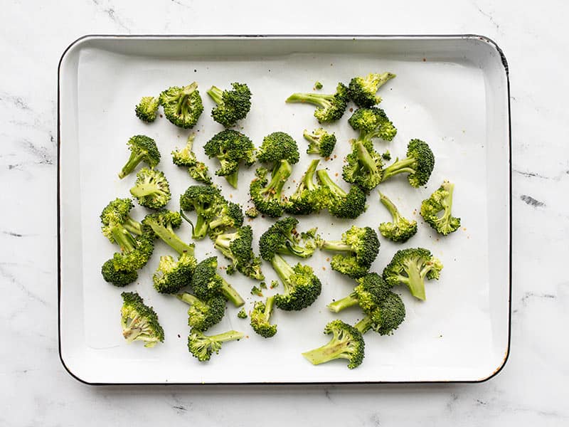 Seasoned broccoli florets on the baking sheet