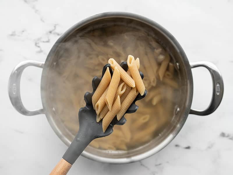 Cooked whole wheat penne being held in a pasta spoon over the pot