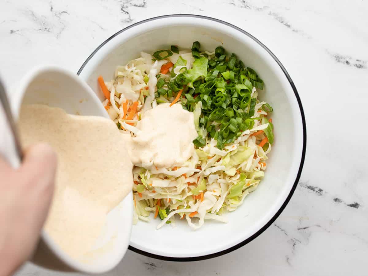 Cumin lime slaw ingredients in a bowl, dressing being poured