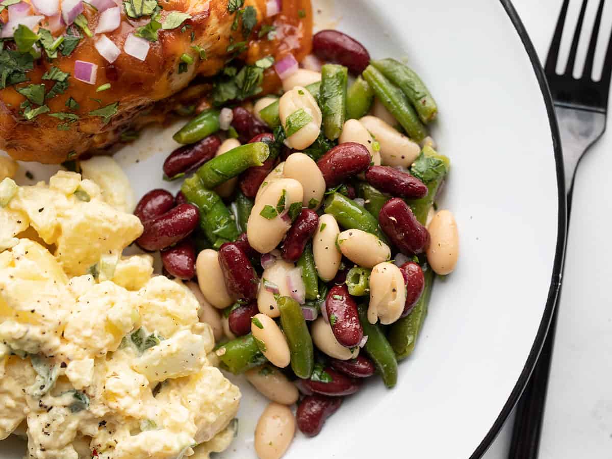 Classic three bean salad on a plate with chicken and potato salad