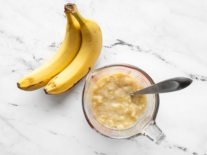 Mashed bananas in a measuring cup next to whole bananas
