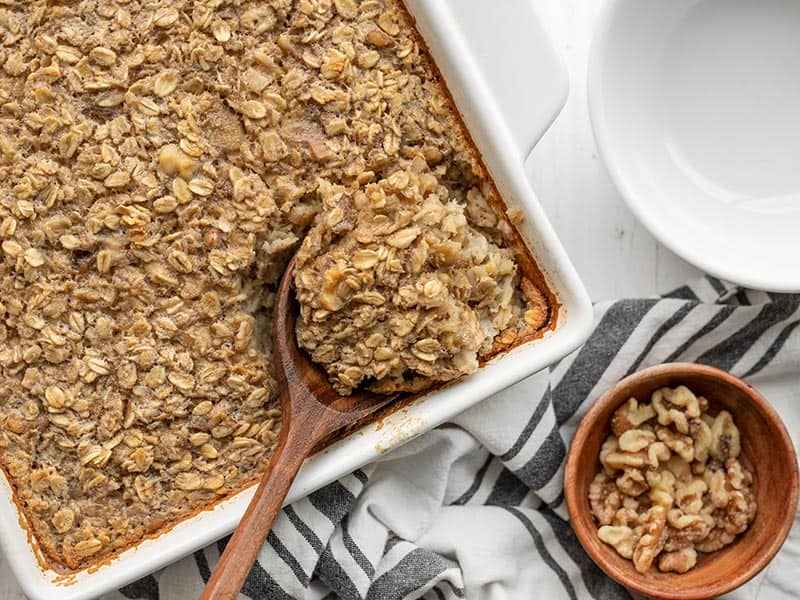 A wooden spoon scooping baked oatmeal out of the side of the casserole dish