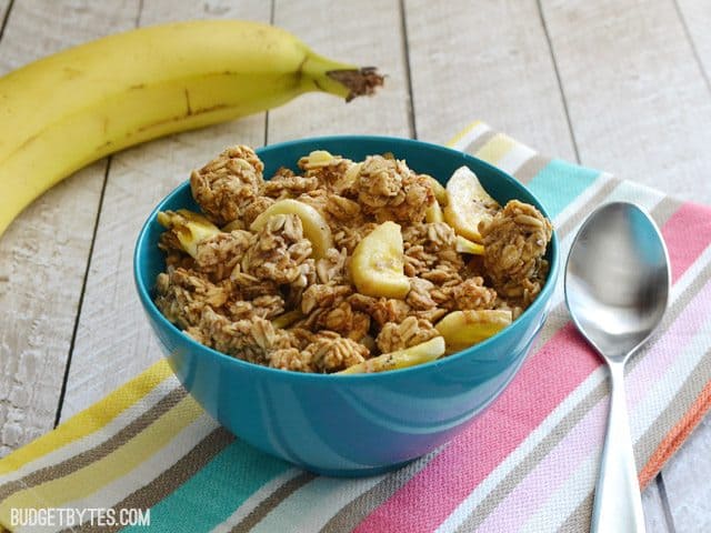 Side view of a bowl of Banana Nut Granola sitting on a colorful napkin, whole banana and spoon on the side 