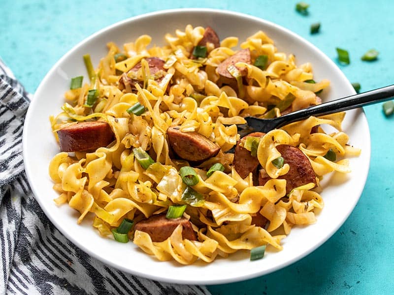 Front view of a bowl of Cajun Cabbage and Noodles with a black fork. 