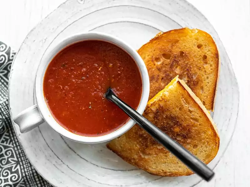 Overhead view of a mug full of tomato soup with a black spoon in the center