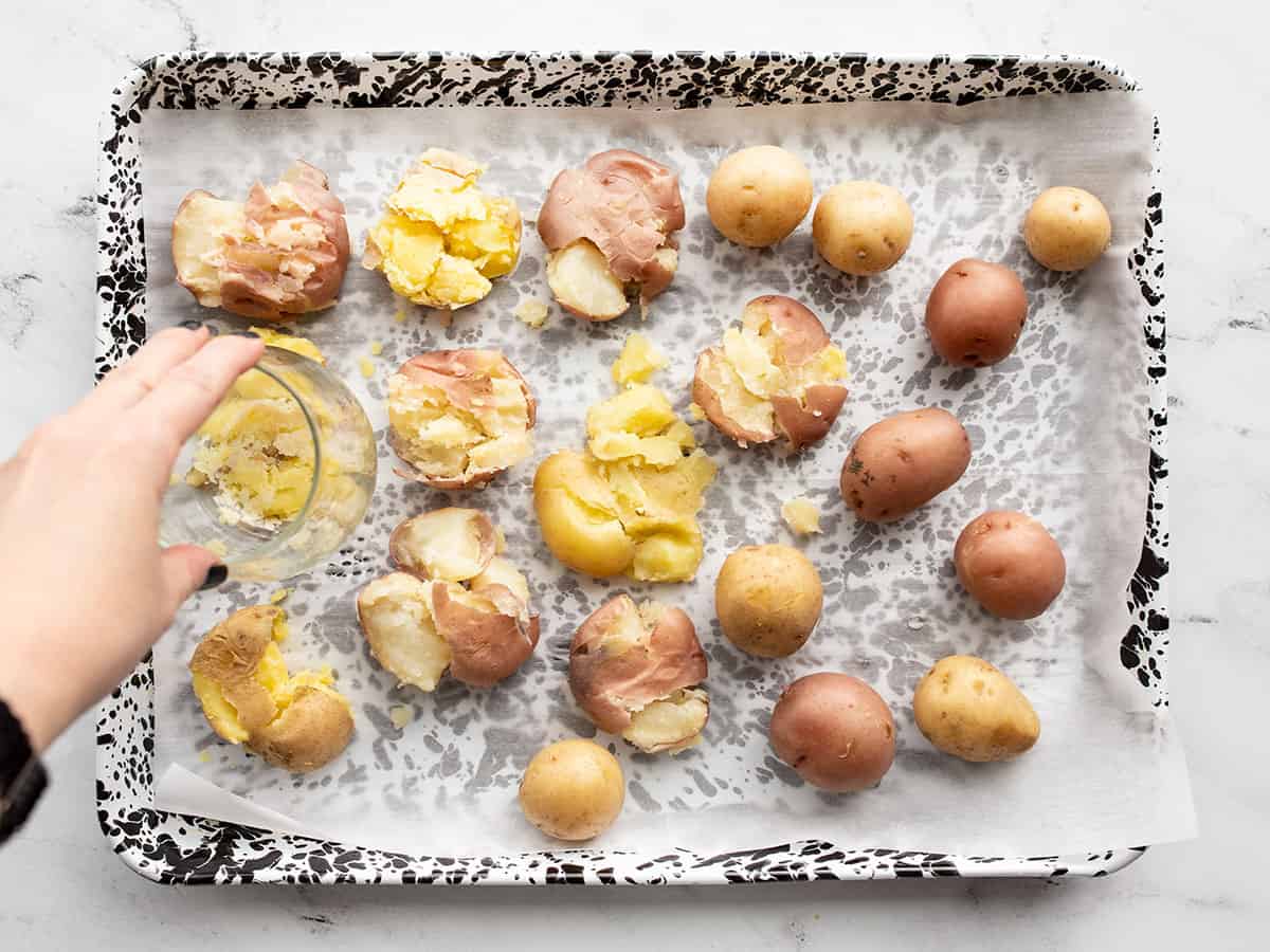 boiled potatoes on the baking sheet being smashed with a glass