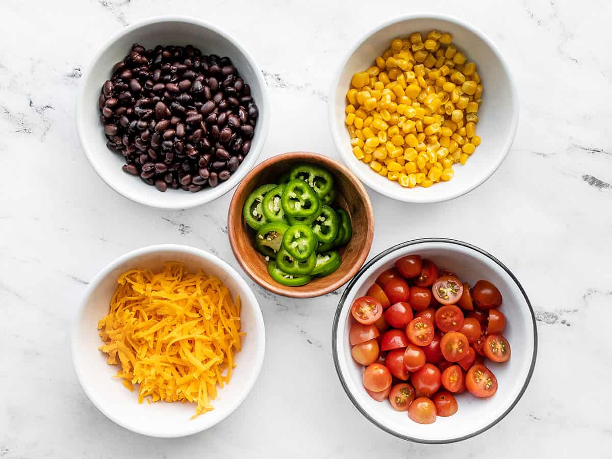 turkey taco salad toppings in bowls: beans, corn, cheese, tomatoes, jalapeño