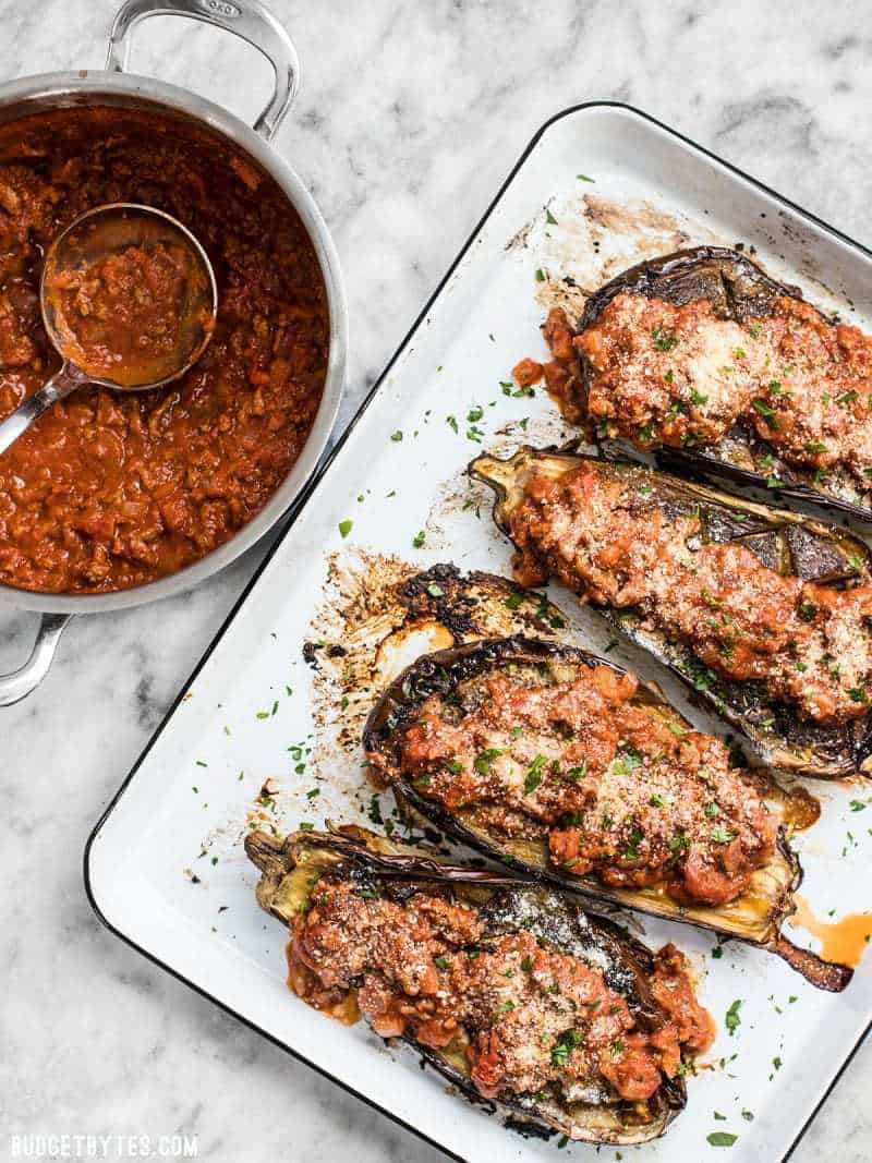 Four Roasted Eggplant with Meat Sauce on a baking sheet next to a pot full of meat sauce. 