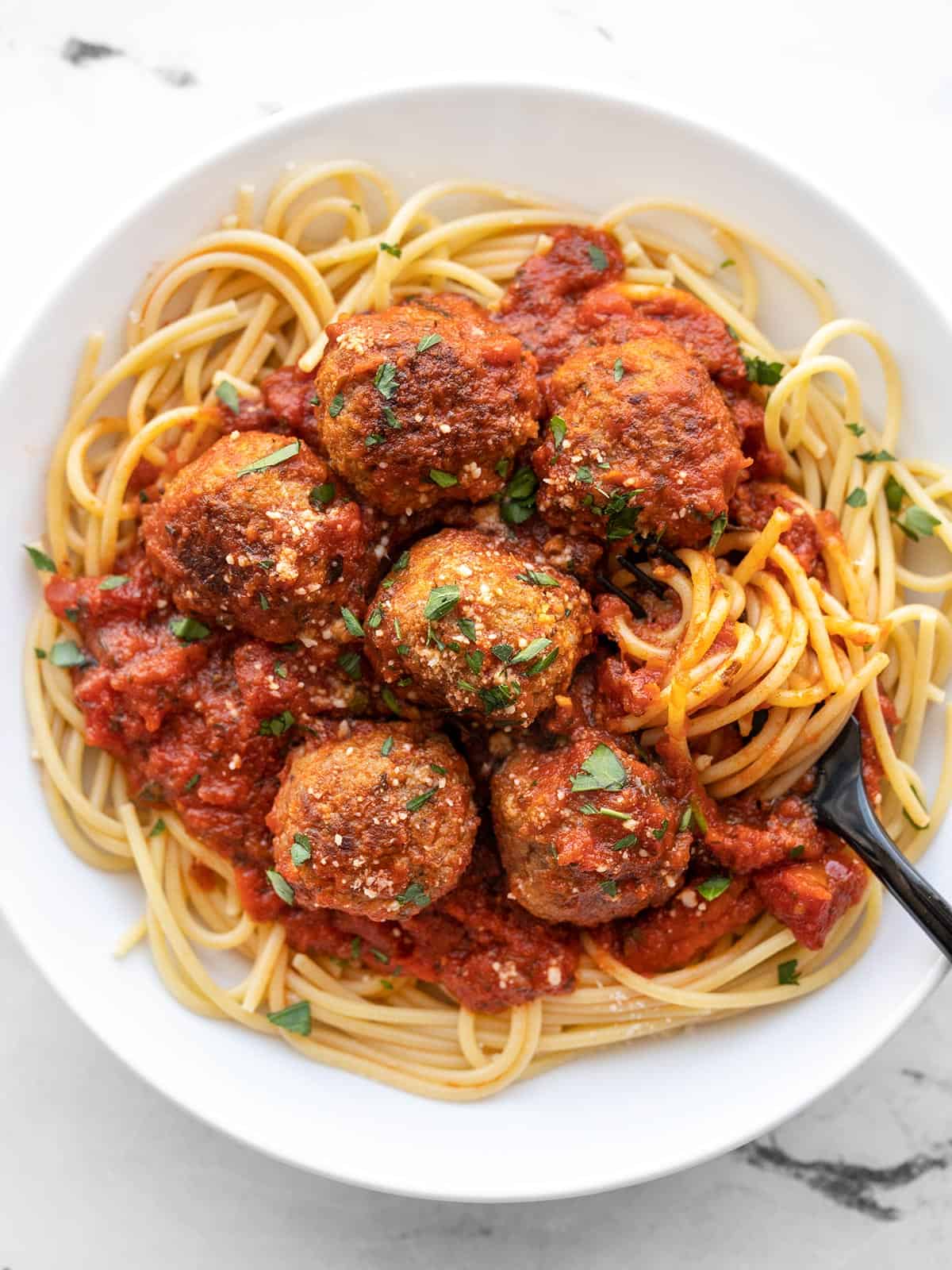 A plate full of spaghetti and meatballs with a fork twirling the pasta