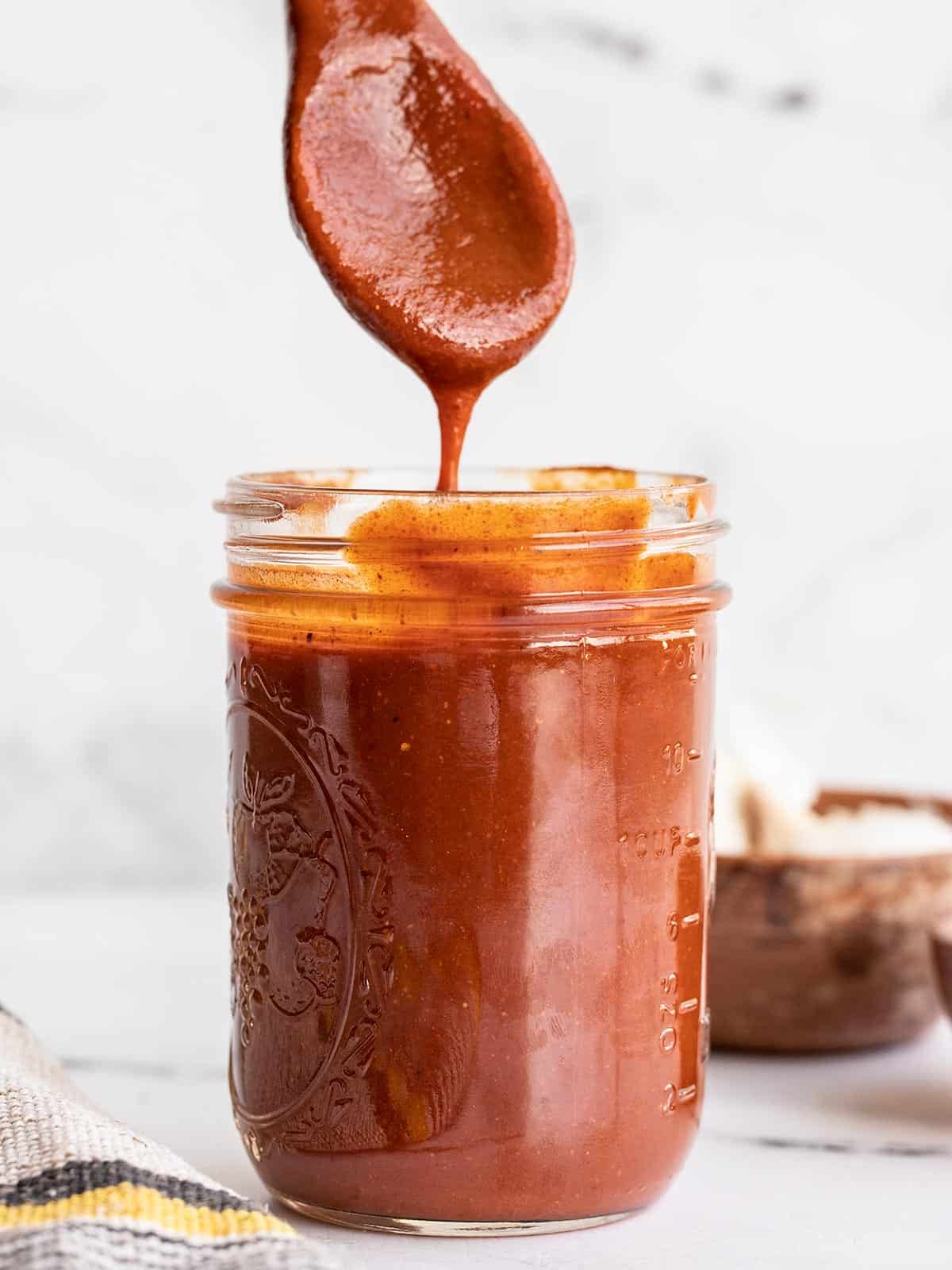 red enchilada sauce dripping from a wooden spoon into a glass jar.