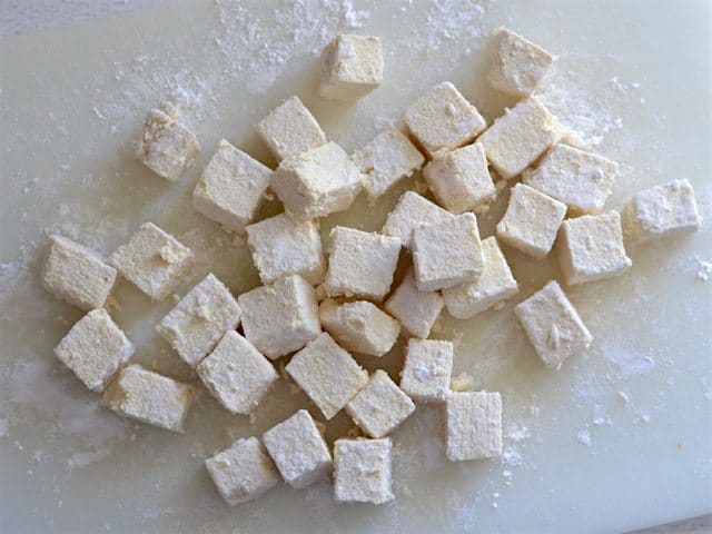 Cubed tofu coated in cornstarch on a cutting board