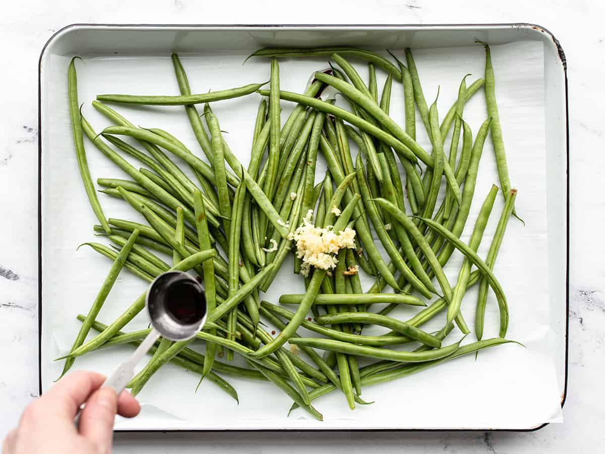 green beans and garlic on a baking sheet, soy sauce being drizzled over top
