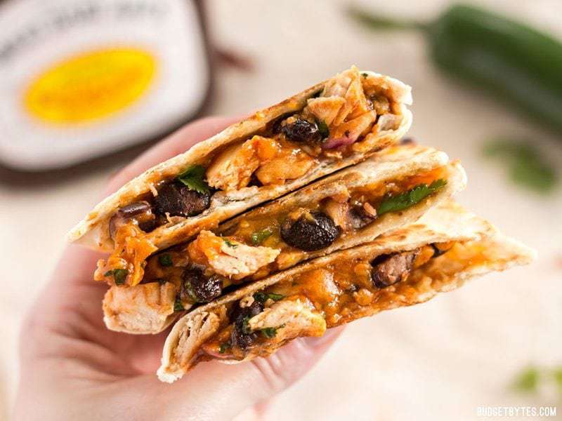 A hand holding three pieces of Ultimate BBQ Chicken Quesadillas stacked