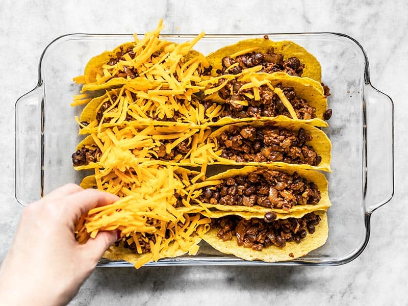 Taco shells being filled with beef and black bean mixture and topped with shredded cheese