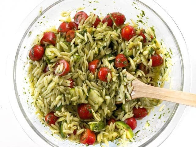 Finished Zucchini and Orzo Salad with Chimichurri in a bowl with a wooden spoon