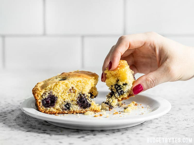 A hand taking a piece of Lemon Blueberry Cornbread from a plate.