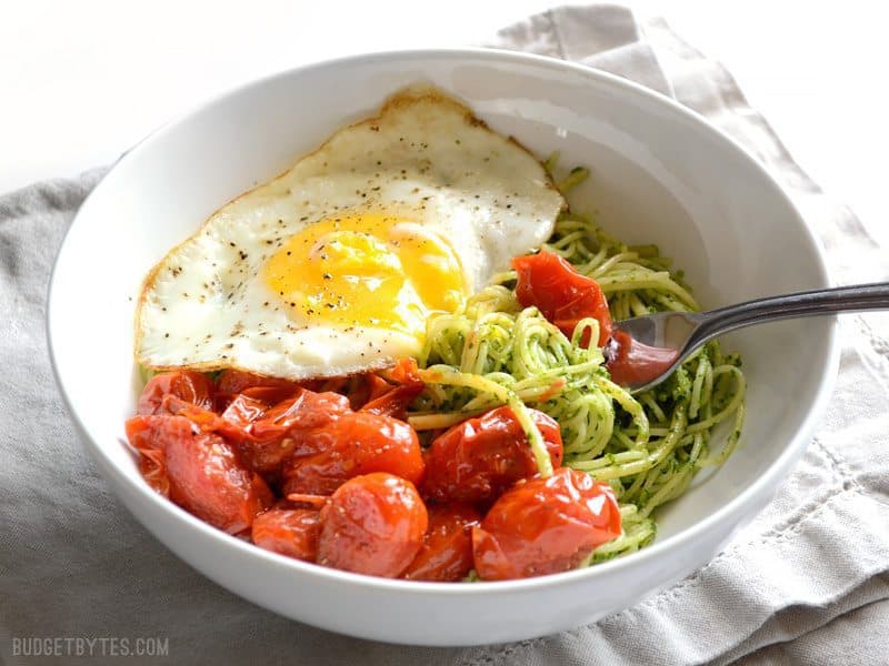 Side view of a bowl of parsley pesto pasta with blistered tomatoes and a fried egg on top